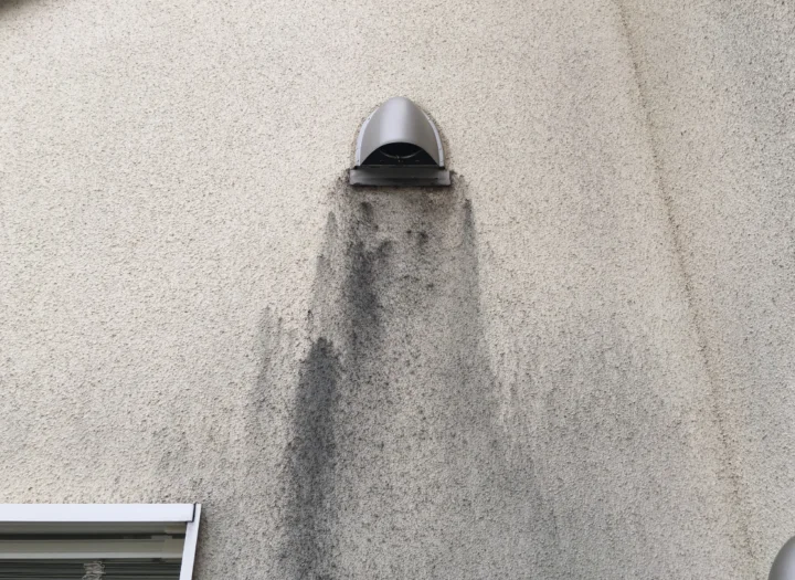 換気口の下に黒い雨だれ汚れが付着した外壁